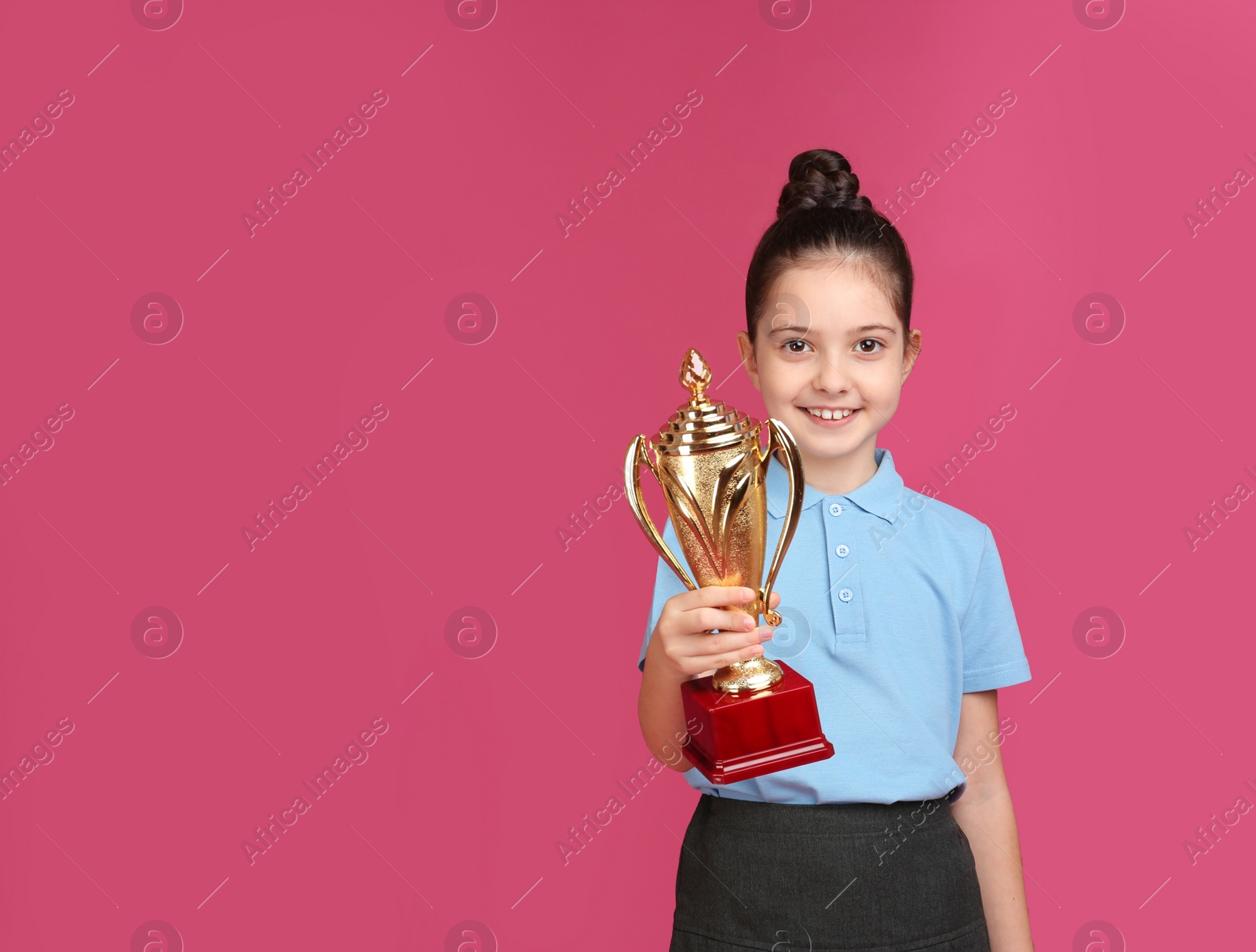 Photo of Happy girl in school uniform with golden winning cup on pink background. Space for text