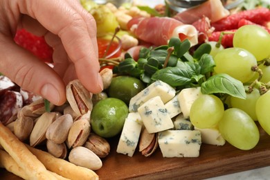 Photo of Woman taking pistachio from board with different appetizers, closeup