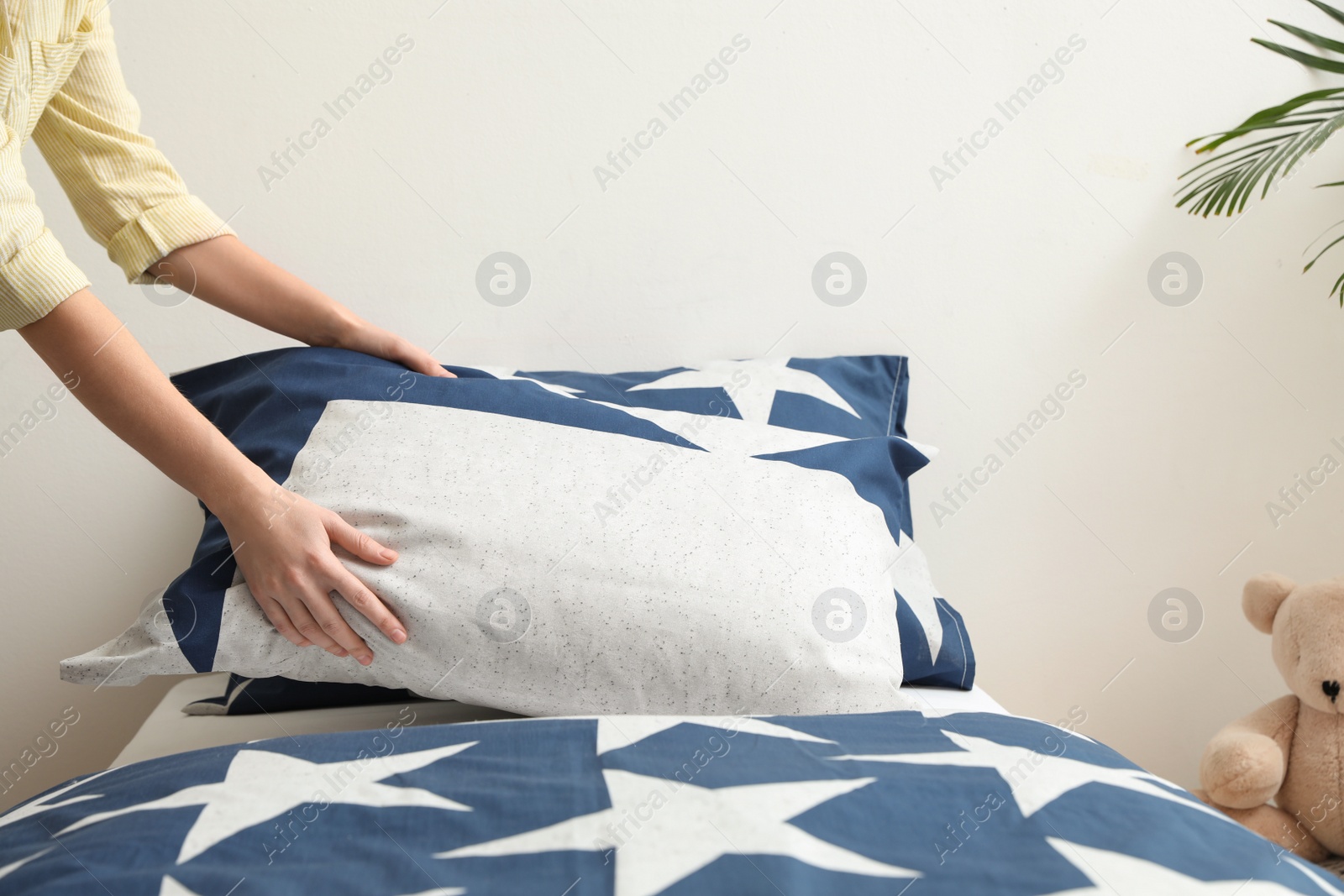Photo of Woman making bed with stylish linens in children's room, closeup