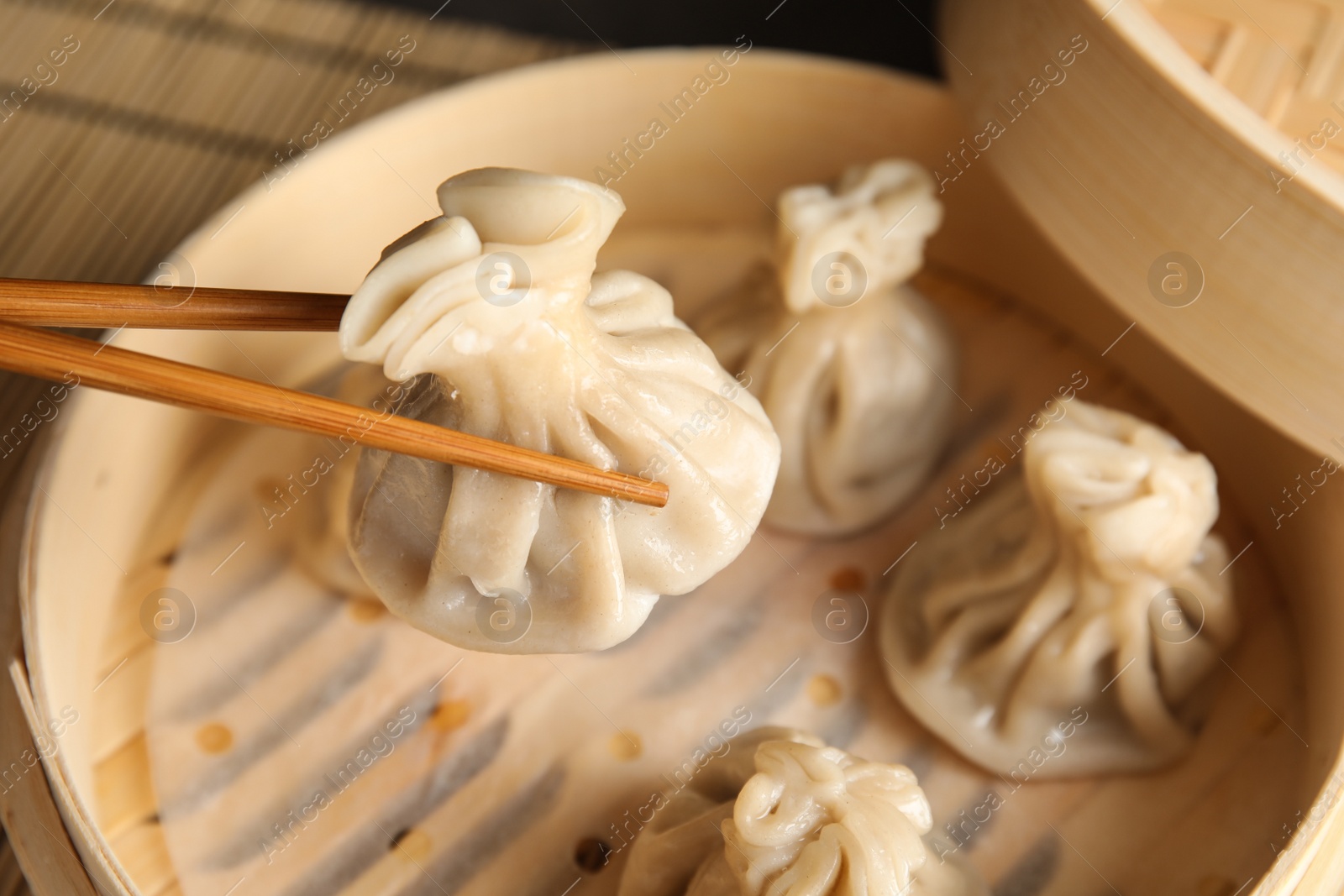 Photo of Chopsticks with baozi dumpling over bamboo steamer, closeup