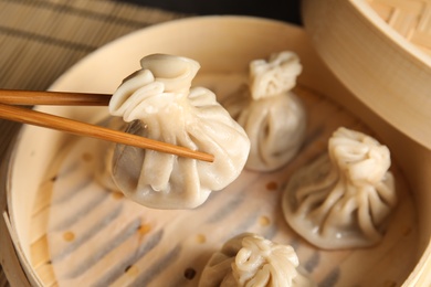 Chopsticks with baozi dumpling over bamboo steamer, closeup