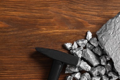 Pile of silver nuggets and hammer on wooden table, flat lay. Space for text