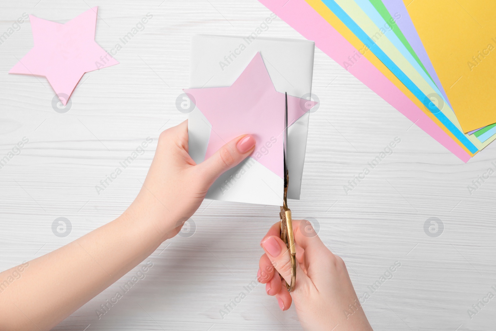 Photo of Woman cutting paper with scissors at white wooden table, top view