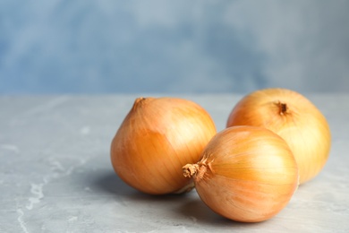 Photo of Ripe onions on grey table against blue background, space for text