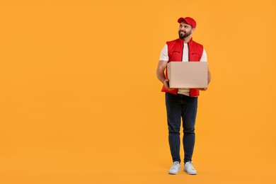 Photo of Happy young courier with parcel on orange background. Space for text