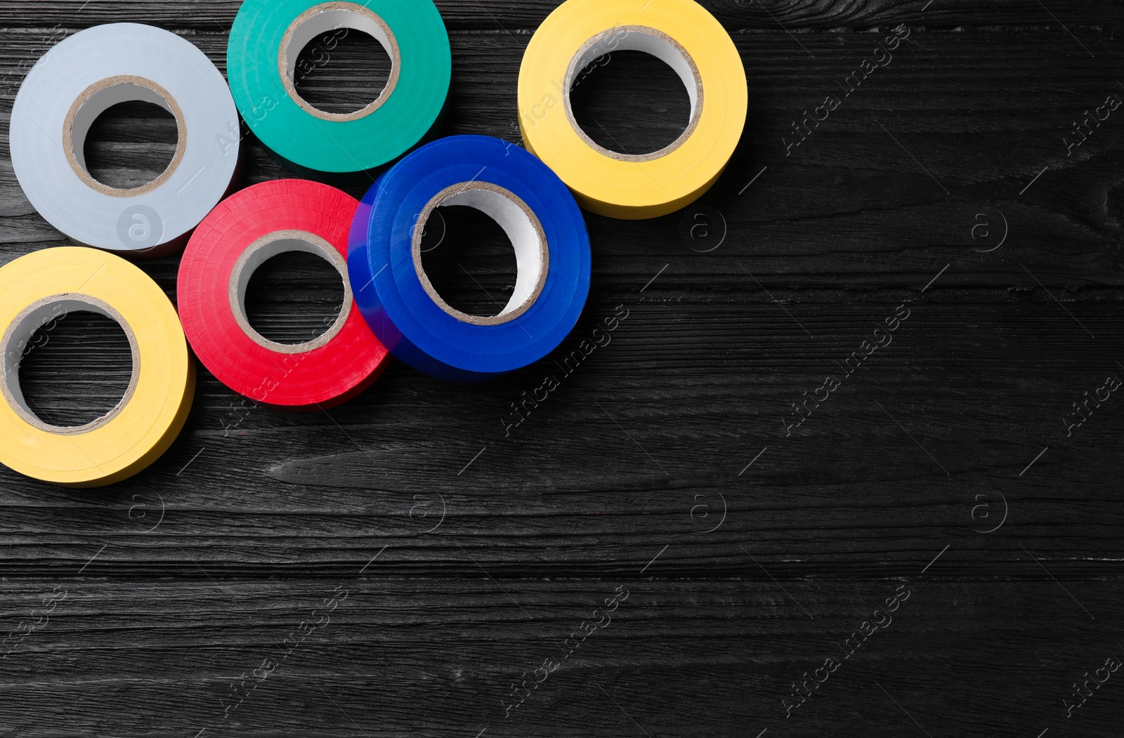 Photo of Colorful insulating tapes on black wooden table, flat lay. Space for text