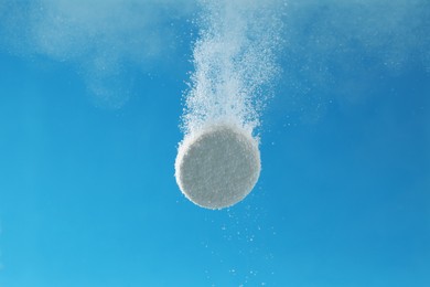 Photo of Effervescent pill dissolving in water on light blue background, closeup