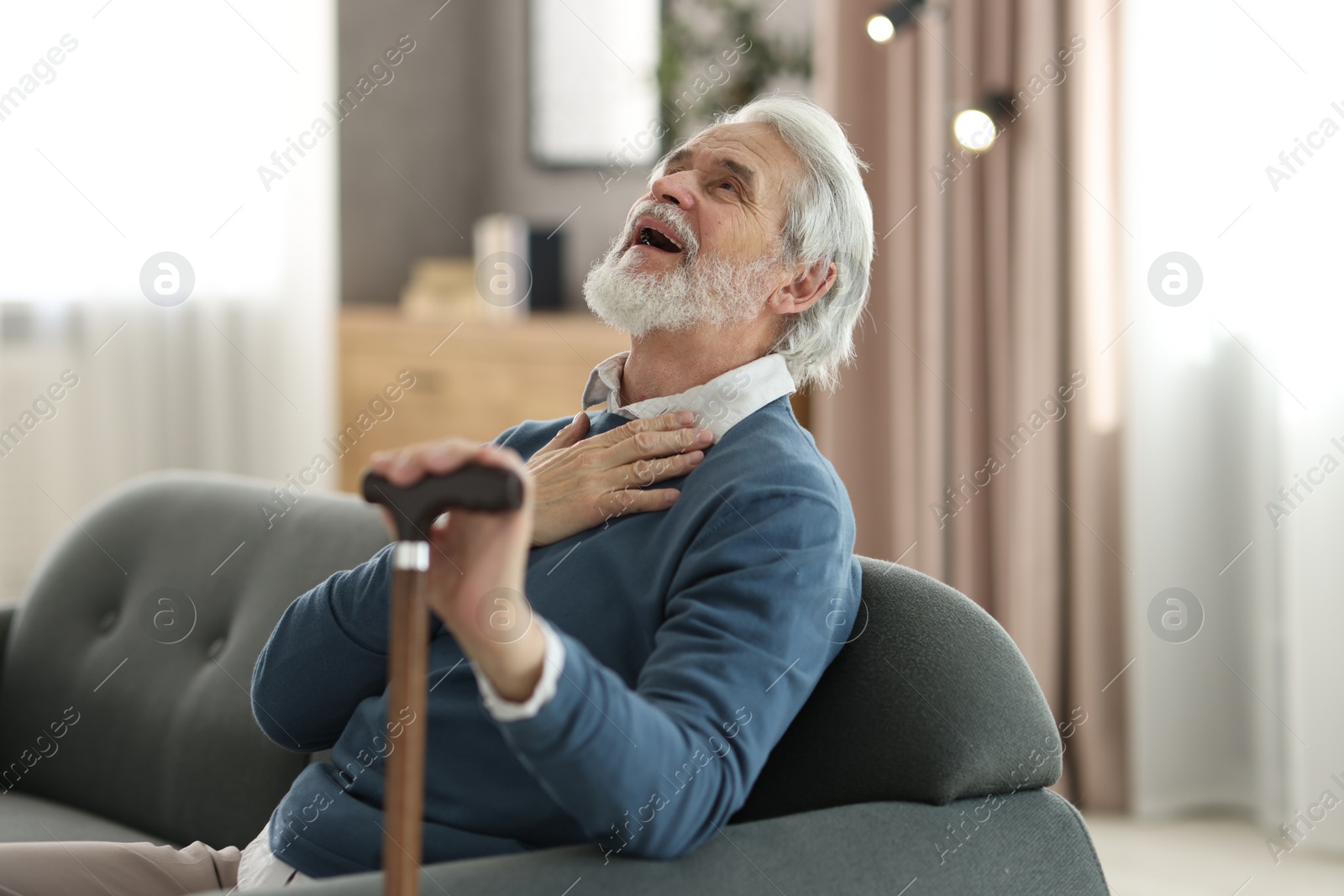 Photo of Portrait of happy grandpa with walking cane sitting on sofa indoors