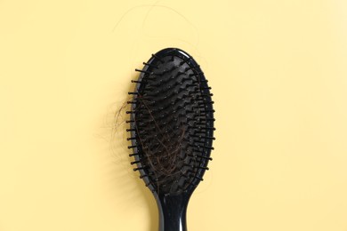 Photo of Brush with lost hair on yellow background, top view