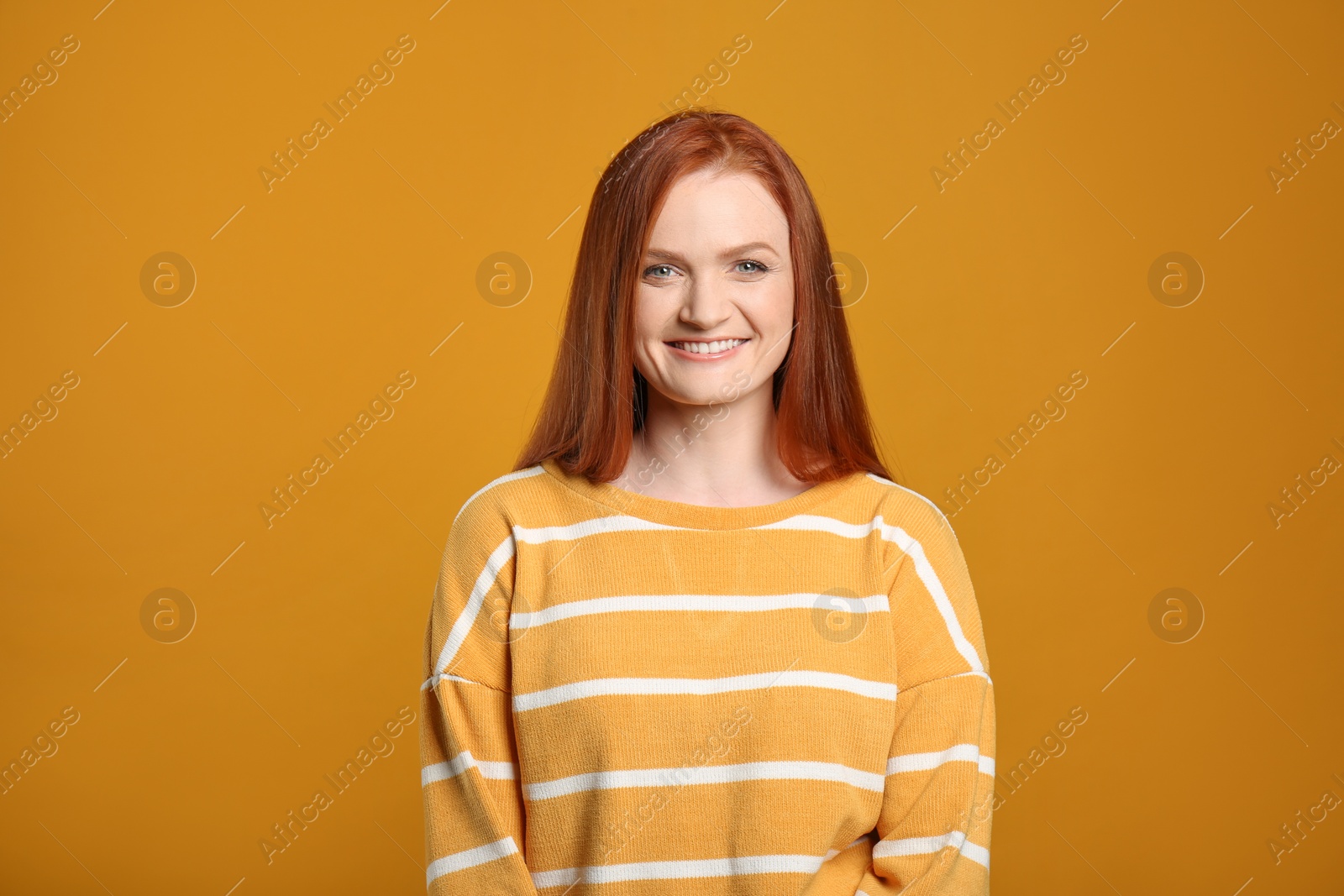 Photo of Candid portrait of happy young woman with charming smile and gorgeous red hair on yellow background