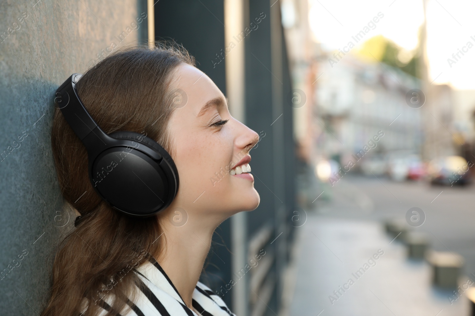 Photo of Smiling woman in headphones listening to music near building outdoors. Space for text