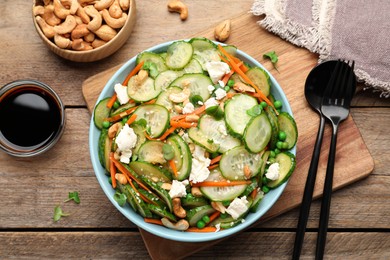 Photo of Bowl of delicious cucumber salad served on wooden table, flat lay