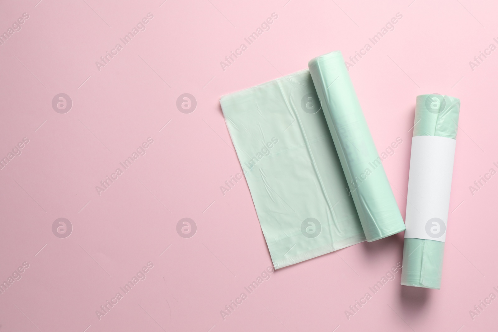 Photo of Rolls of garbage bags on pink background, flat lay. Space for text