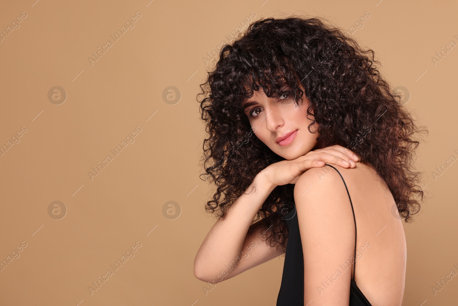 Photo of Beautiful young woman with long curly hair on beige background. Space for text