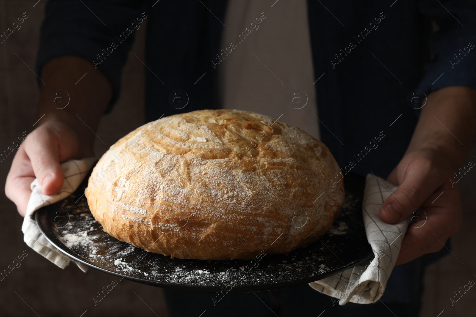 Photo of Man holding loaf of fresh bread on dark background, closeup