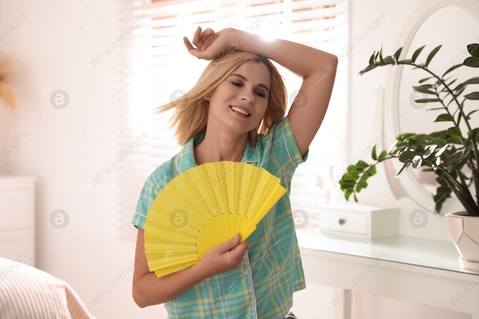 Photo of Woman enjoying air flow from hand fan at home. Summer heat