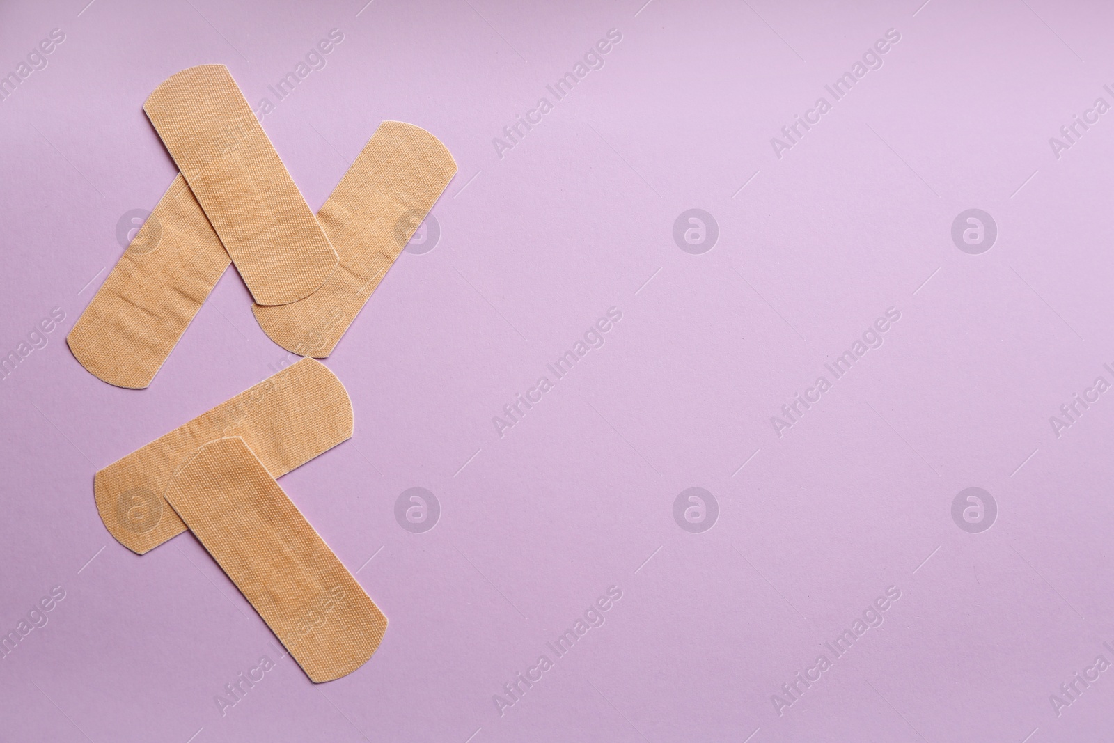 Photo of Sticking plasters on lilac background, flat lay. Space for text
