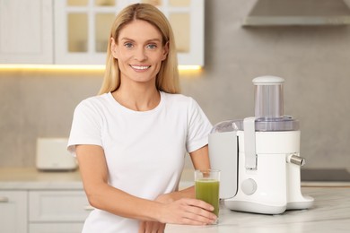 Photo of Happy woman with glass of fresh celery juice at table in kitchen