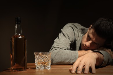 Photo of Addicted man and alcoholic drink at wooden table against dark background, focus on glass
