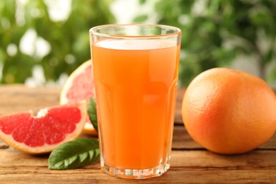 Photo of Glass of delicious grapefruit juice on wooden table against blurred background