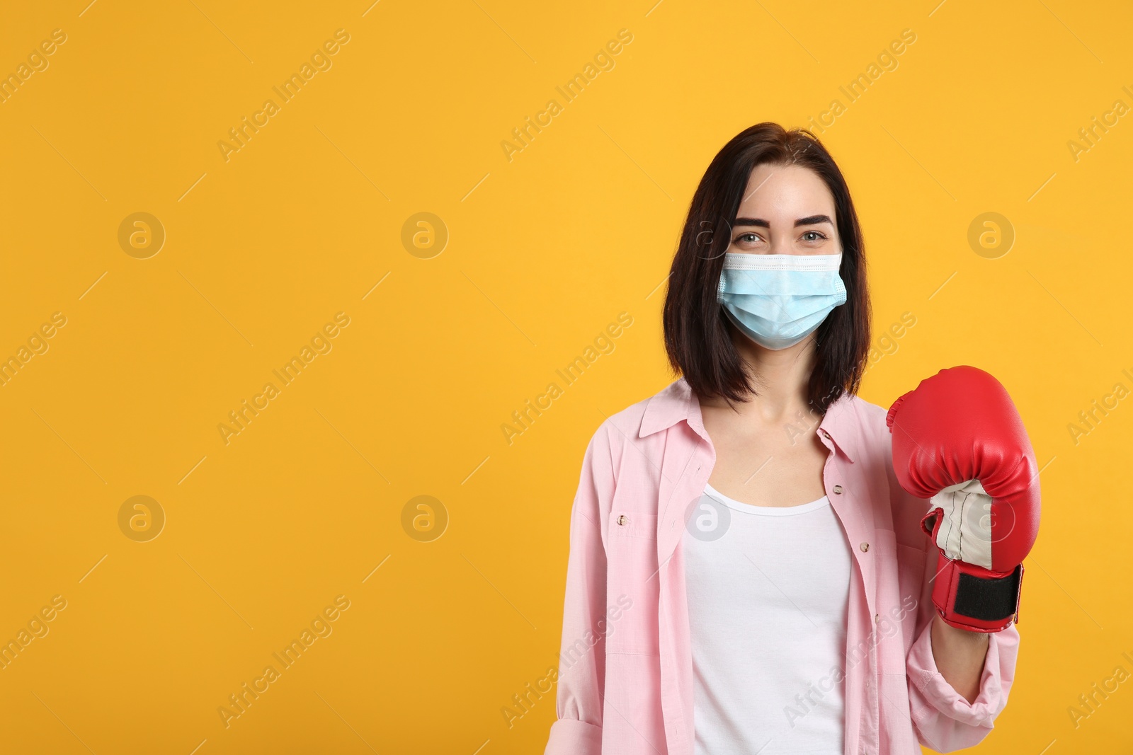 Photo of Woman with protective mask and boxing gloves on yellow background, space for text. Strong immunity concept