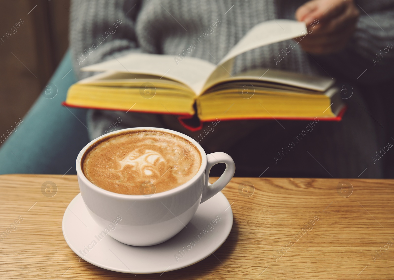 Image of Woman reading book in cafe, focus on cup of coffee