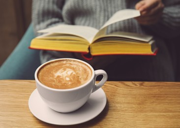 Woman reading book in cafe, focus on cup of coffee