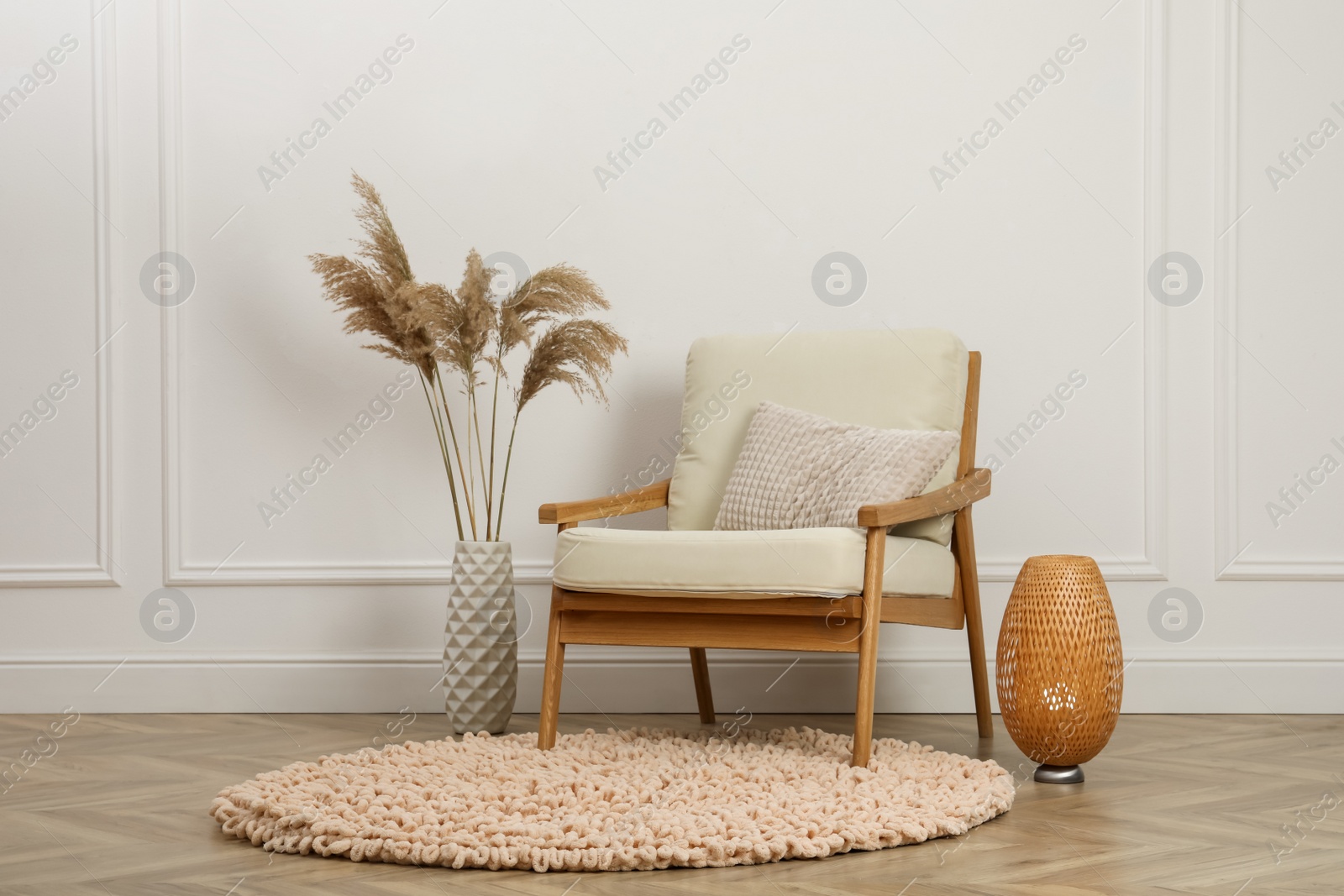 Photo of Stylish armchair with cushion, spikes and lamp near white wall indoors. Interior design