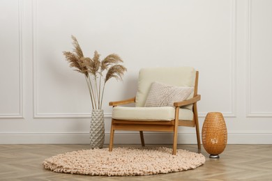 Photo of Stylish armchair with cushion, spikes and lamp near white wall indoors. Interior design