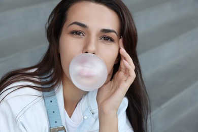 Stylish woman blowing gum near stairs outdoors, closeup