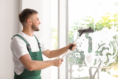 Male cleaner wiping window glass with squeegee indoors