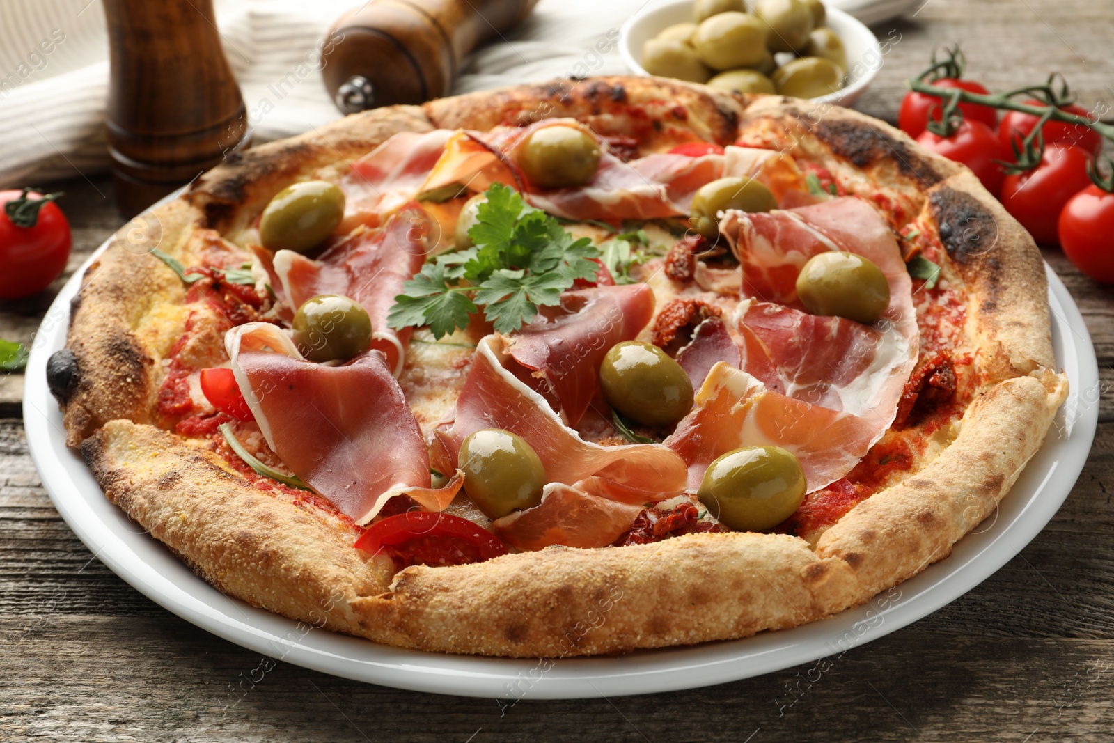 Photo of Tasty pizza with cured ham, olives, tomatoes and parsley on wooden table