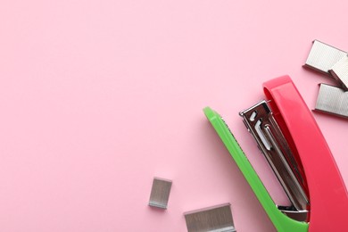 Photo of Bright stapler with staples on pink background, flat lay. Space for text