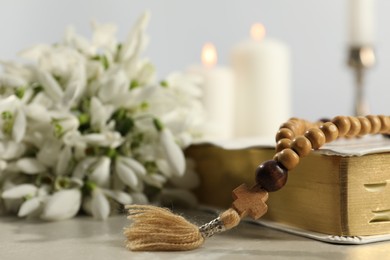 Photo of Bible, rosary beads, flowers and church candles on light table, closeup