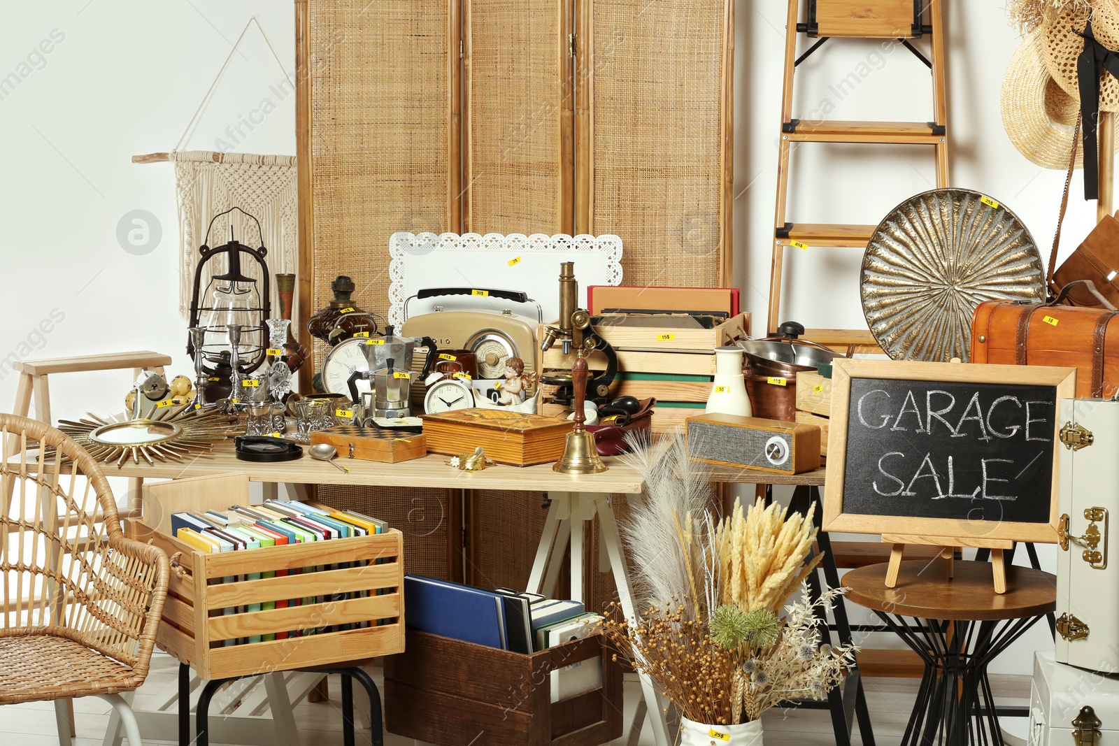 Photo of Sign Garage Sale written on blackboard near many different stuff indoors