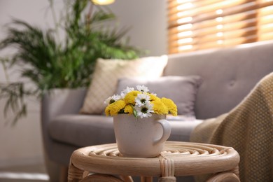 Cup with beautiful bright flowers on table in living room