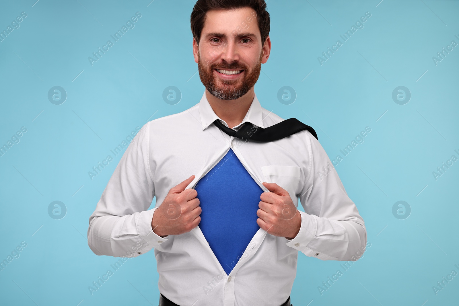 Photo of Happy businessman wearing superhero costume under suit on light blue background