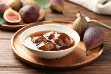 Photo of Bowl of tasty sweet jam and fresh figs on wooden table