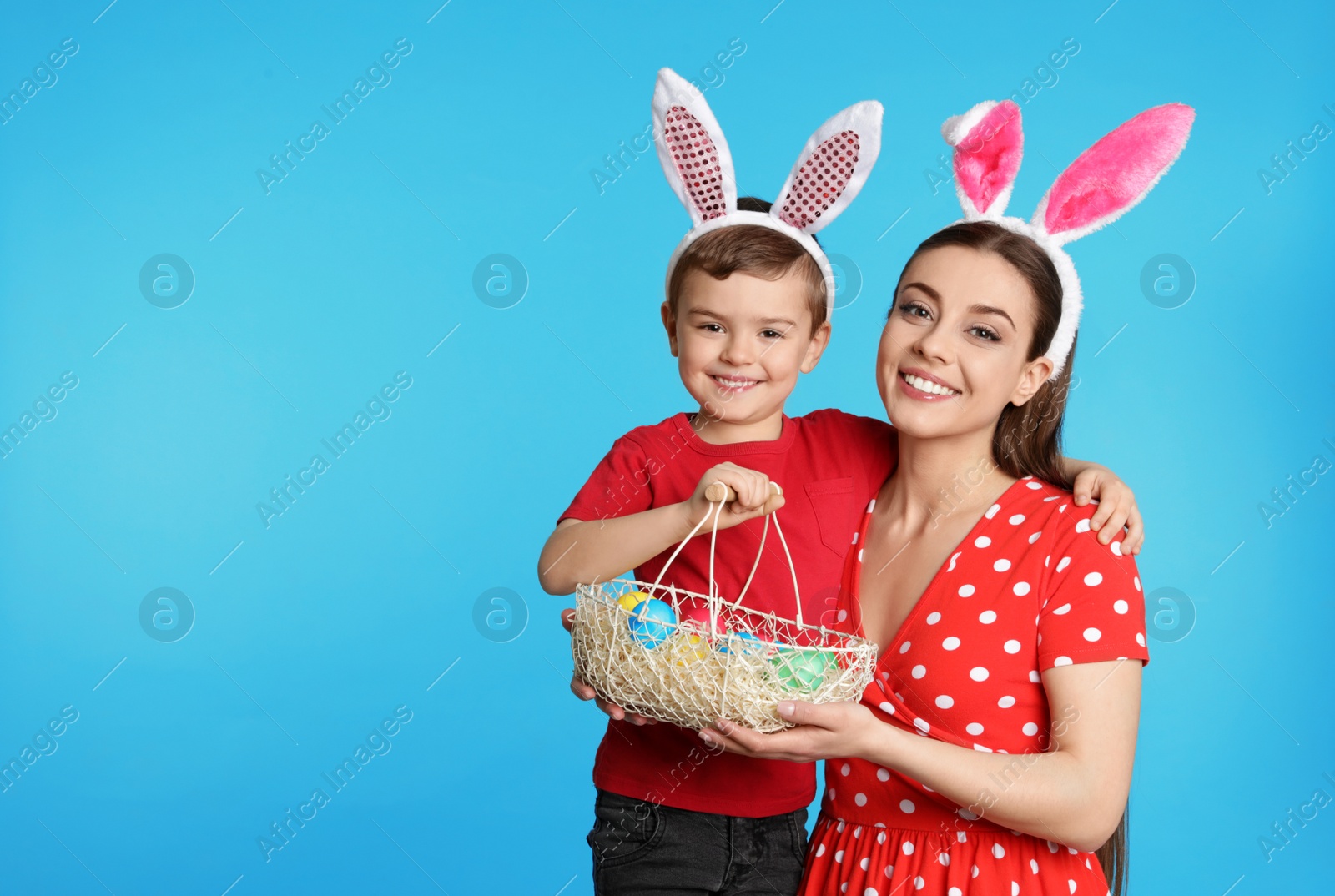 Photo of Mother and son in bunny ears headbands with Easter eggs on color background, space for text