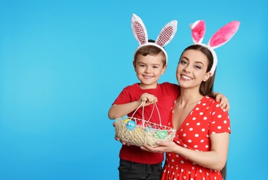 Mother and son in bunny ears headbands with Easter eggs on color background, space for text