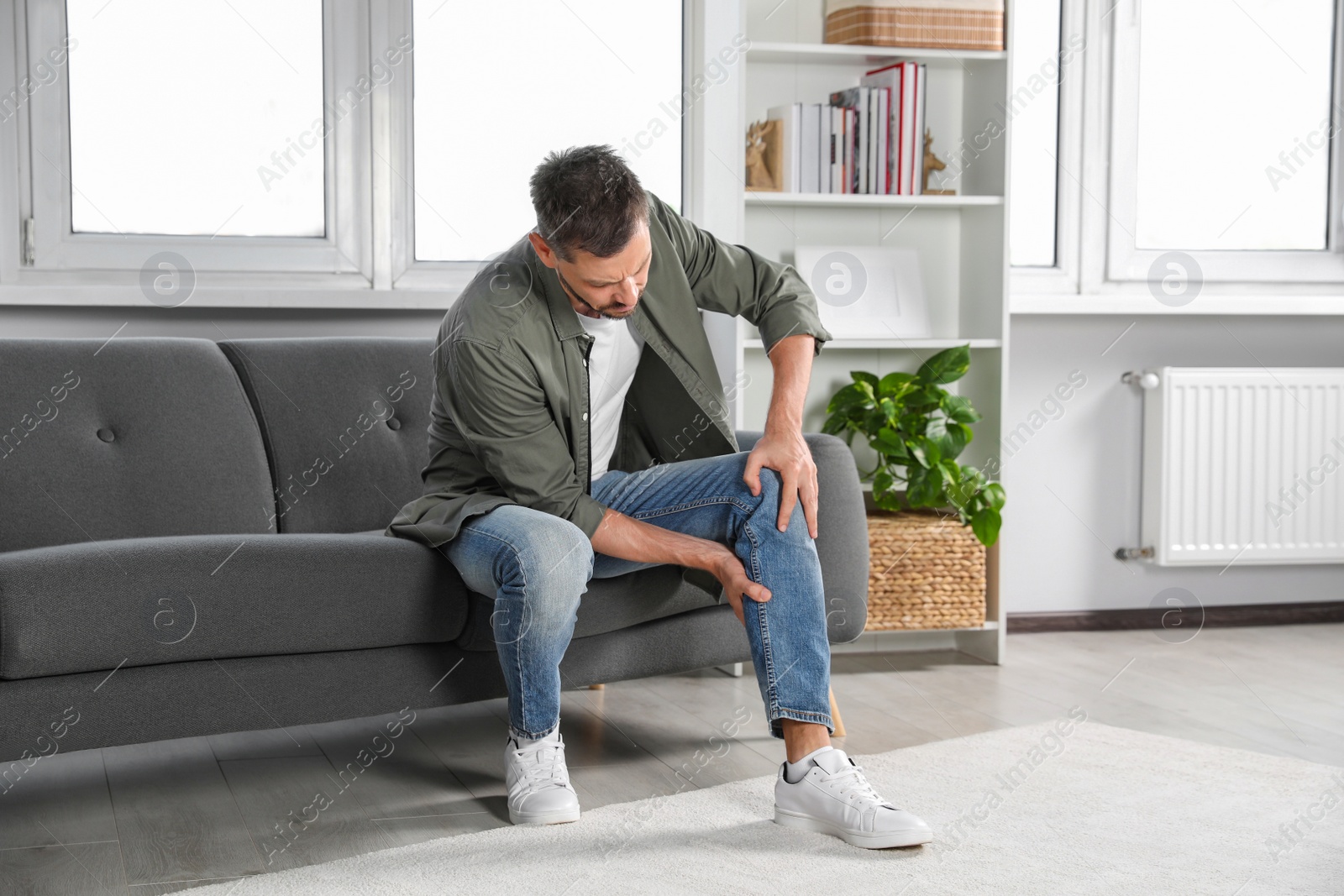 Photo of Man suffering from pain in leg on sofa at home