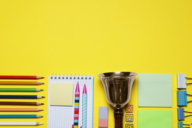 Different stationery and school bell on yellow background, flat lay. Space for text