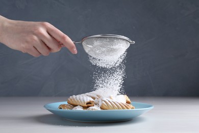 Photo of Woman with sieve sprinkling powdered sugar onto cookies at white wooden table, closeup