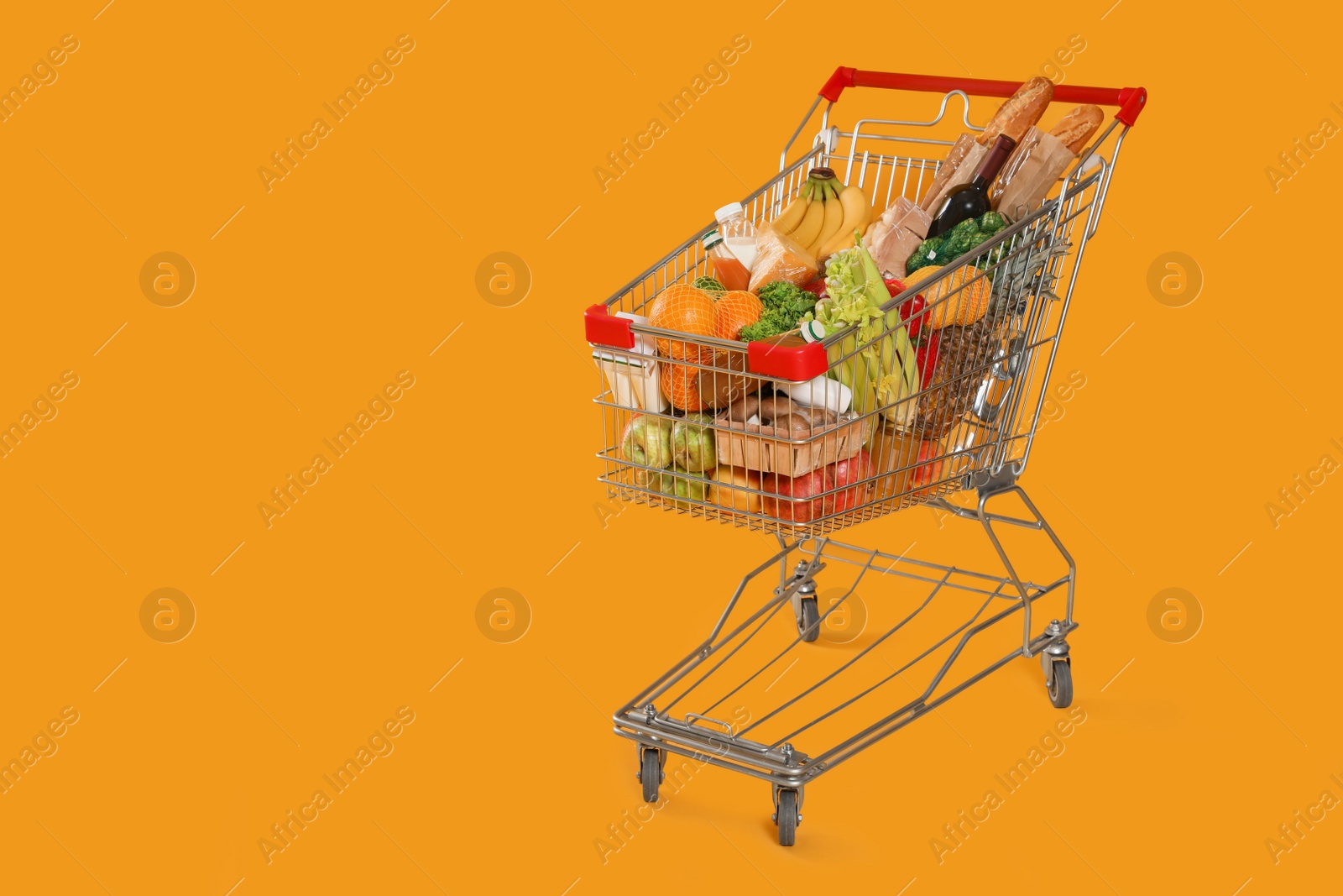 Photo of Shopping cart full of groceries on yellow background. Space for text