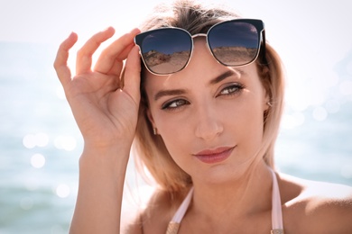 Beautiful woman wearing sunglasses near sea on sunny day, closeup
