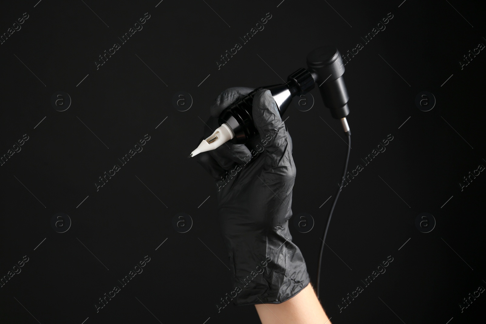 Photo of Professional tattoo artist with machine on black background, closeup