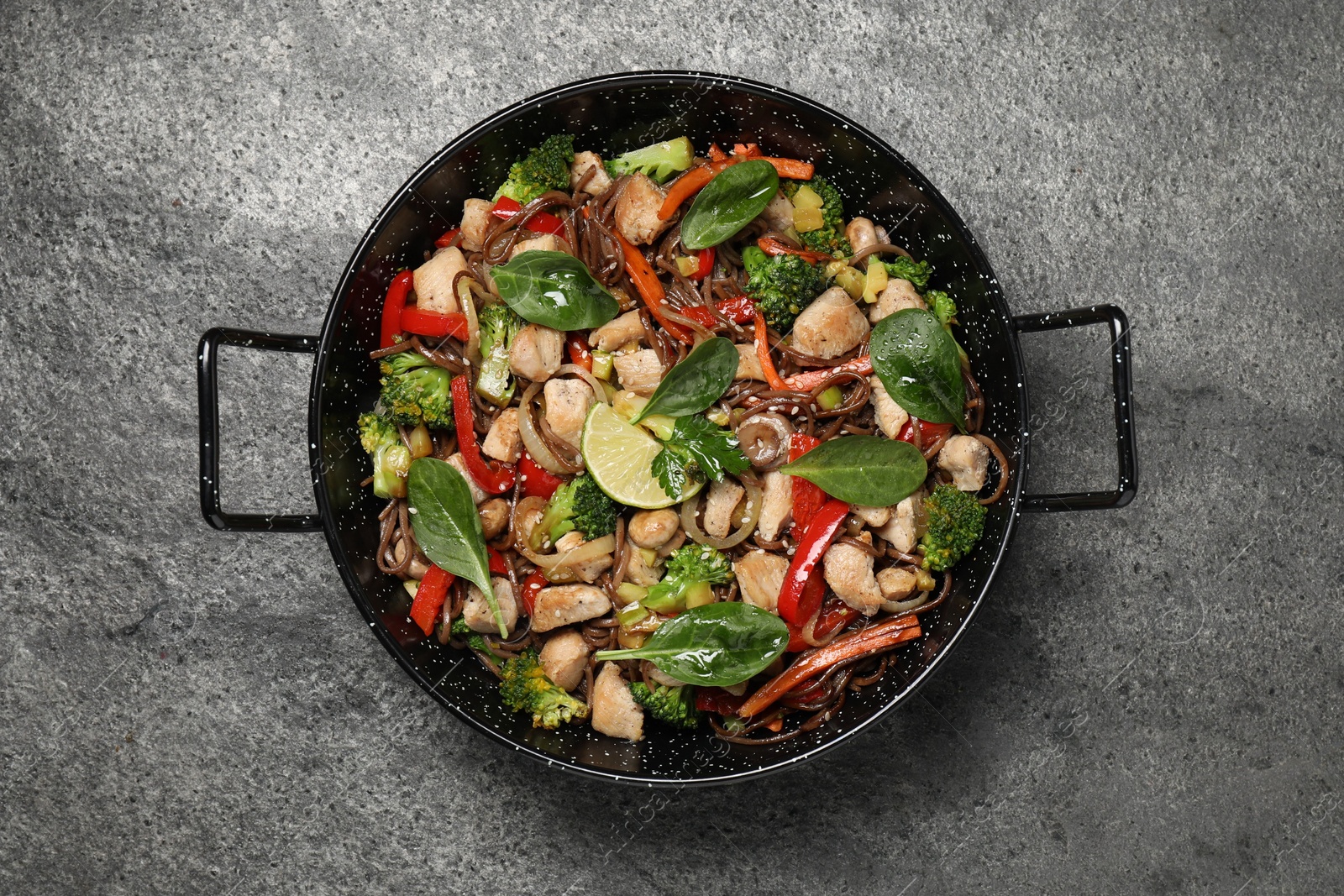 Photo of Stir-fry. Tasty noodles with meat and vegetables in wok on grey textured table, top view