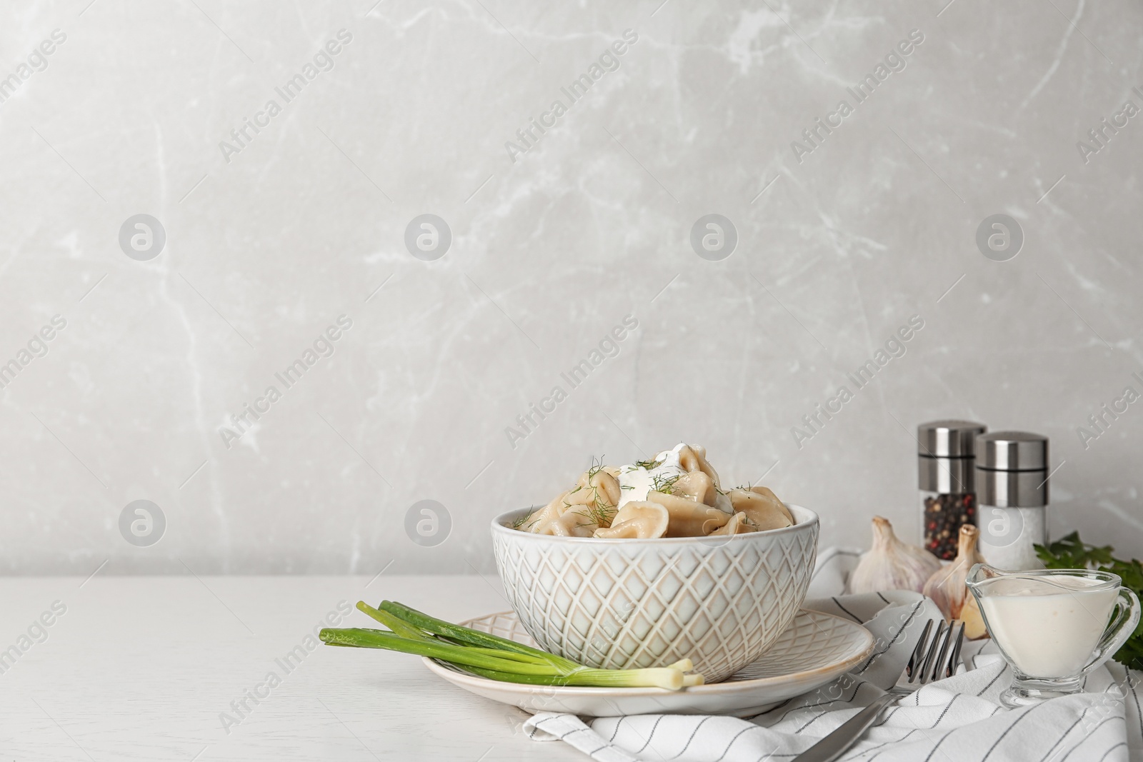 Photo of Tasty dumplings served with sour cream and onion on white table. Space for text