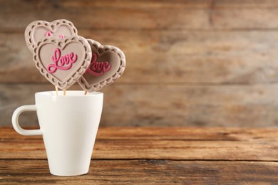 Heart shaped lollipops made of chocolate in cup on wooden table, space for text