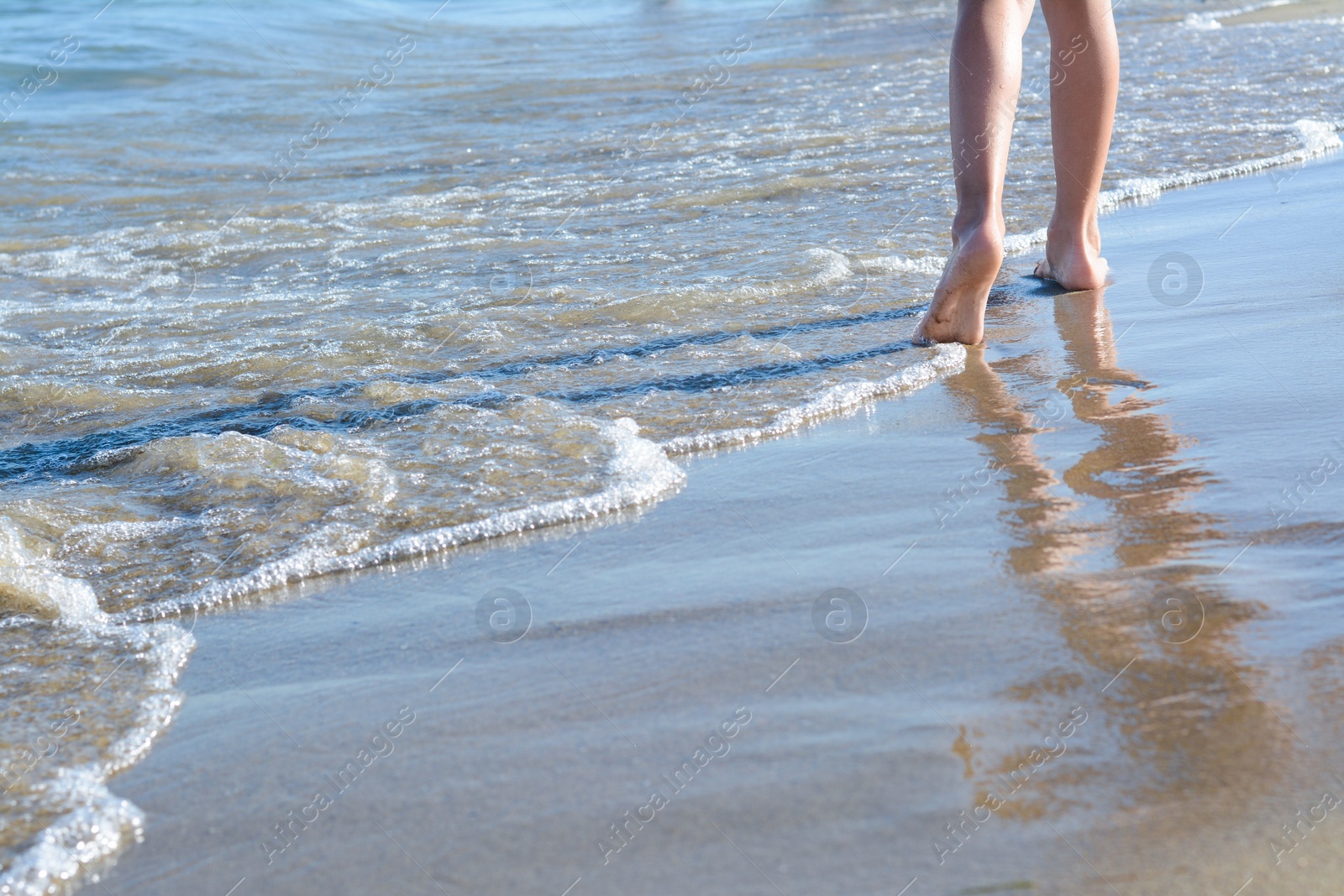 Photo of Child walking through water on seashore, closeup of legs. Space for text